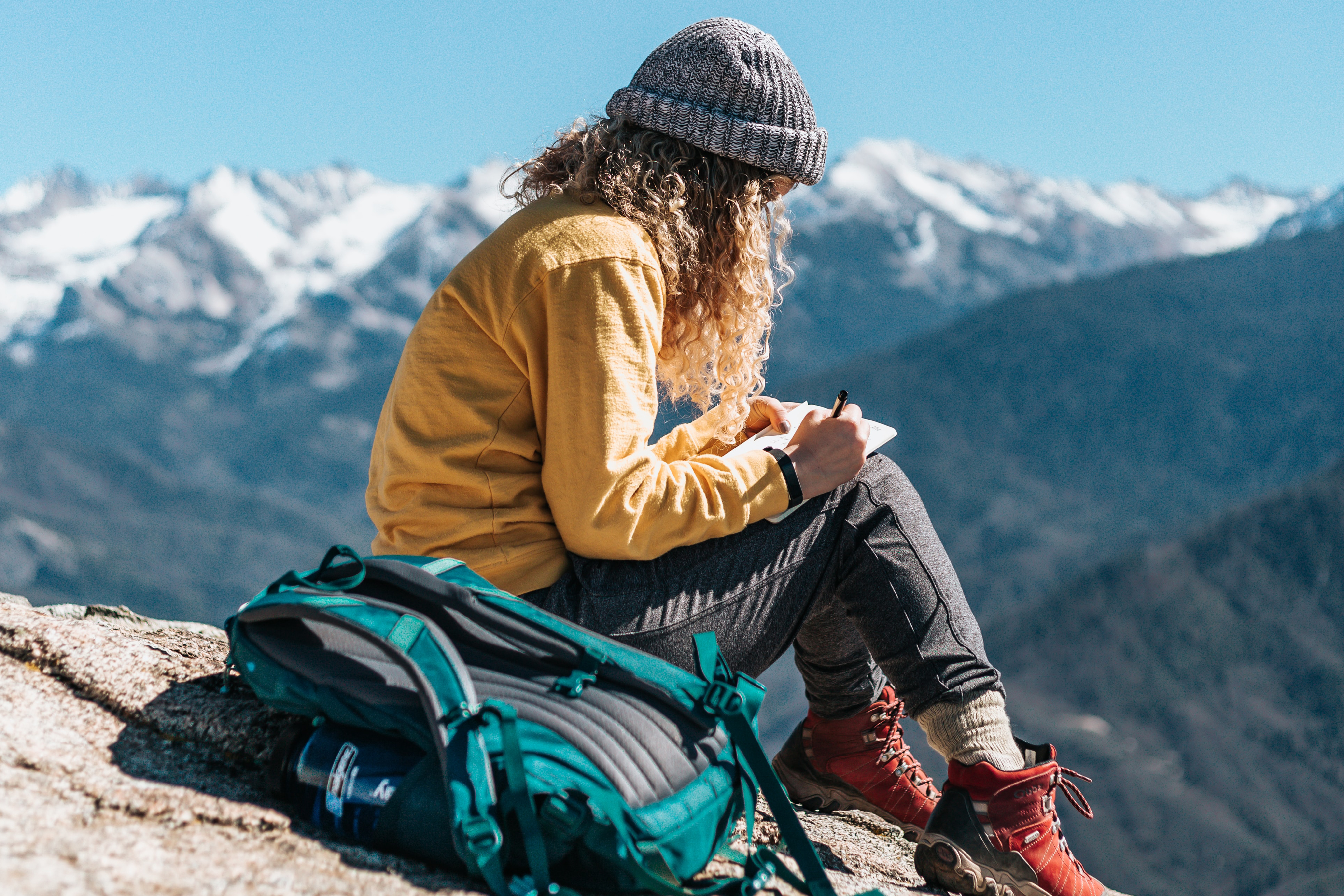 Woman backpacker writing in journal overlooking mountain landscape