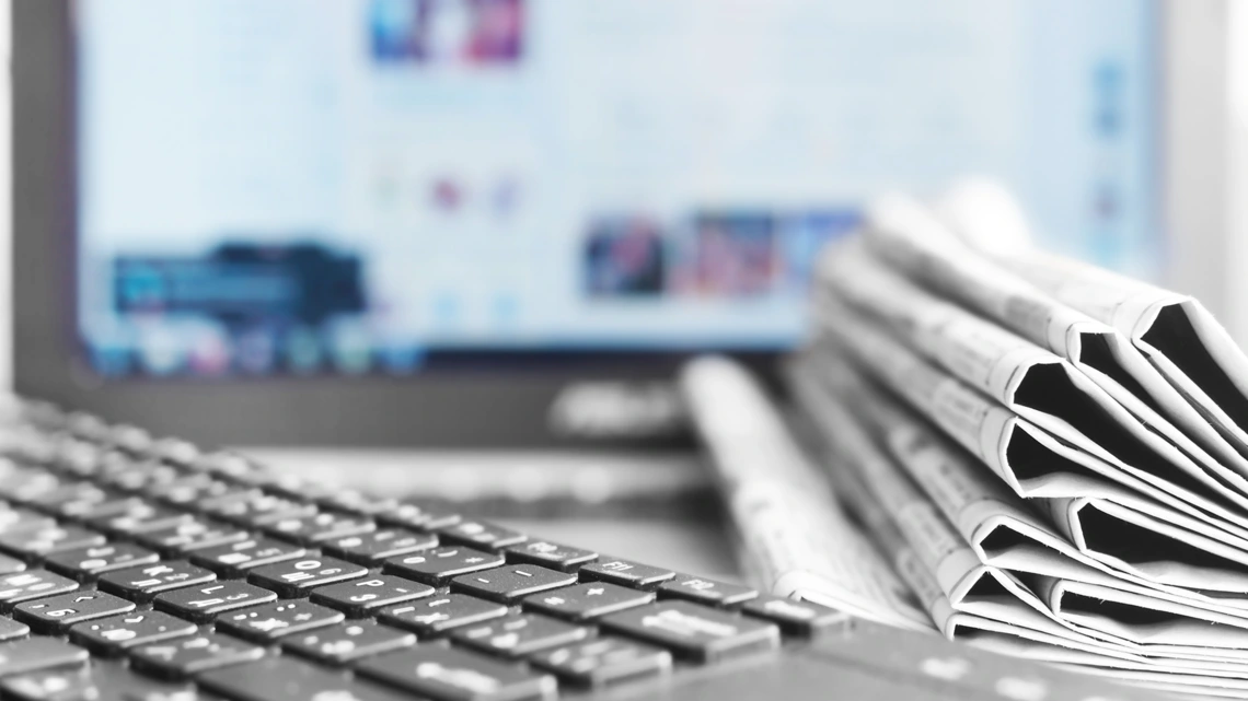 Newspapers and a computer keyboard on a desk.